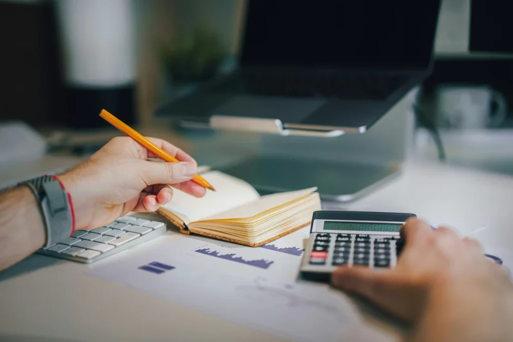 Pessoa a utilizar calculadora e a analisar dados financeiros numa secretária de escritório.