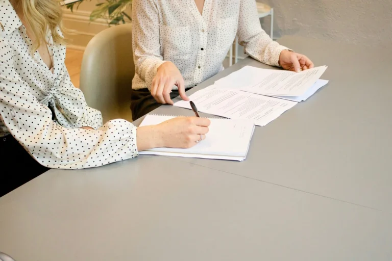 Duas pessoas em reunião a analisar documentos e a tirar notas numa mesa de escritório.